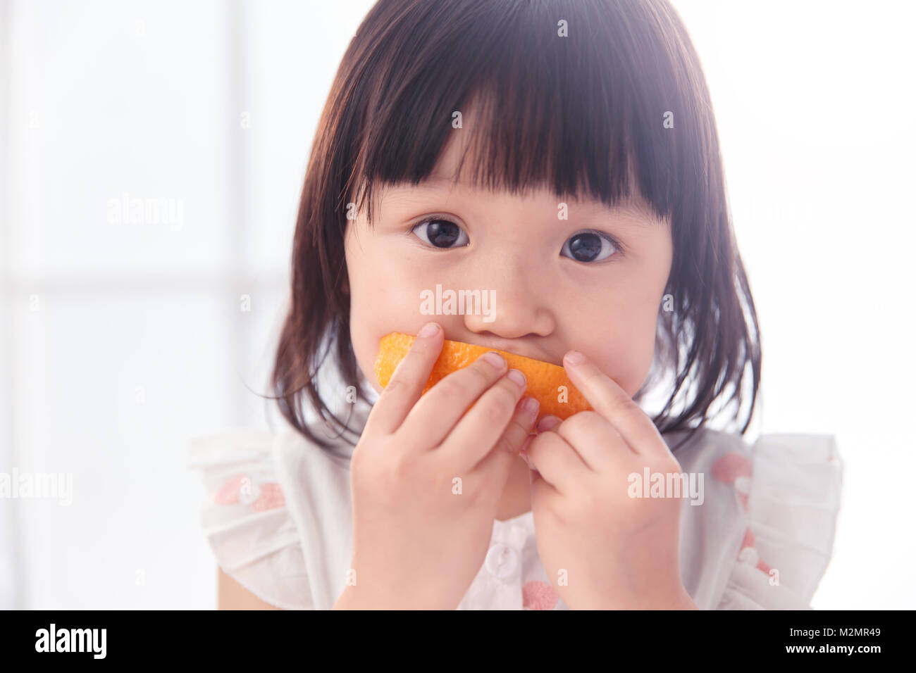The lovely little girl is eating an orange Stock Photo - Alamy