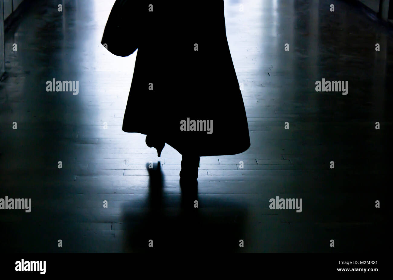 Blurry dark alley in the night with silhouette and shadow of a woman in long coat and high heels walking away Stock Photo