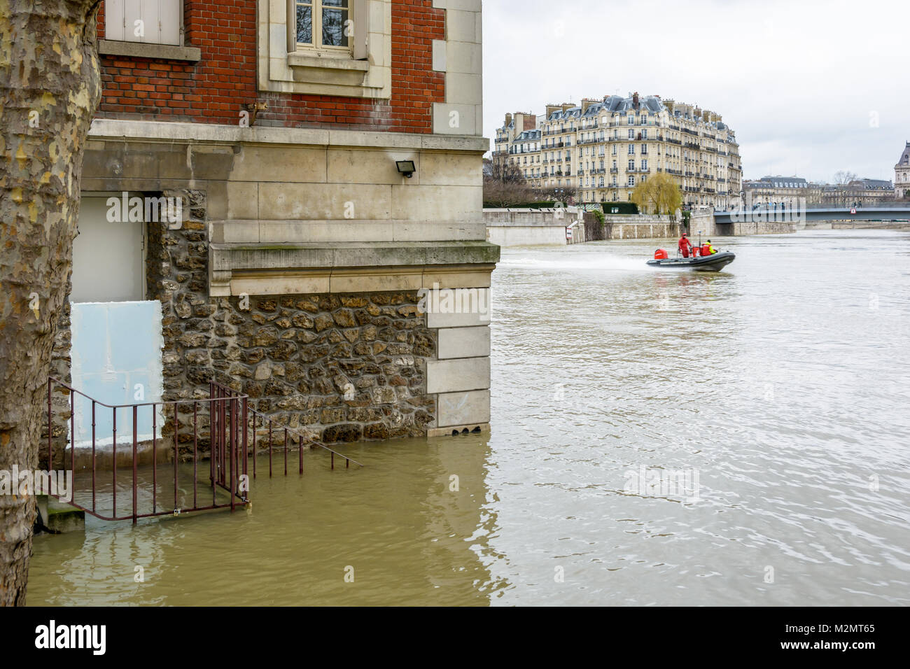 Paris, France - January 29, 2018: Divers from the Paris Fire Brigade on a motorboat pass at full speed in front of a brick house half-submerged by the Stock Photo