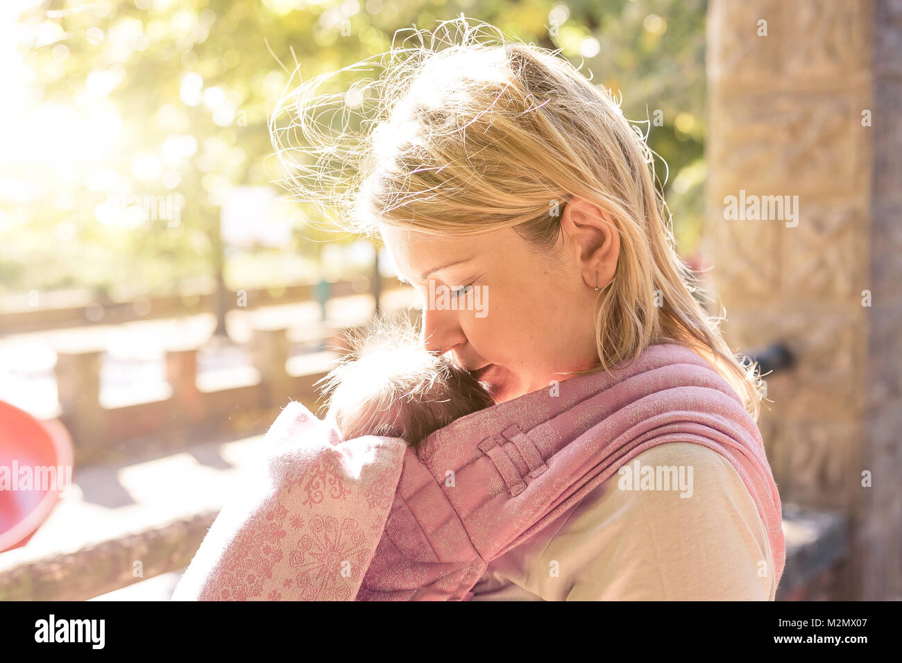 Beautiful Young mother carrying a newborn baby in a pink shawl sling in a sunny day- Concept Young Mothers. Stock Photo