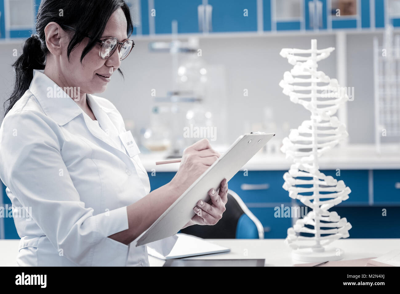 Concentrated mature lady writing something down in laboratory Stock Photo