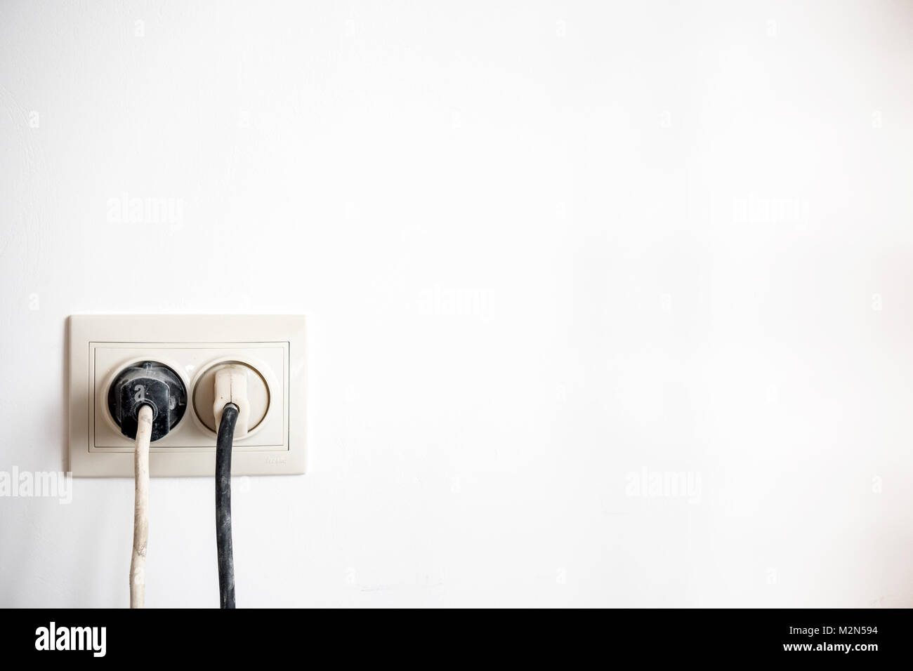 Electric socket with two stuck electric plugs on a white wall. Power