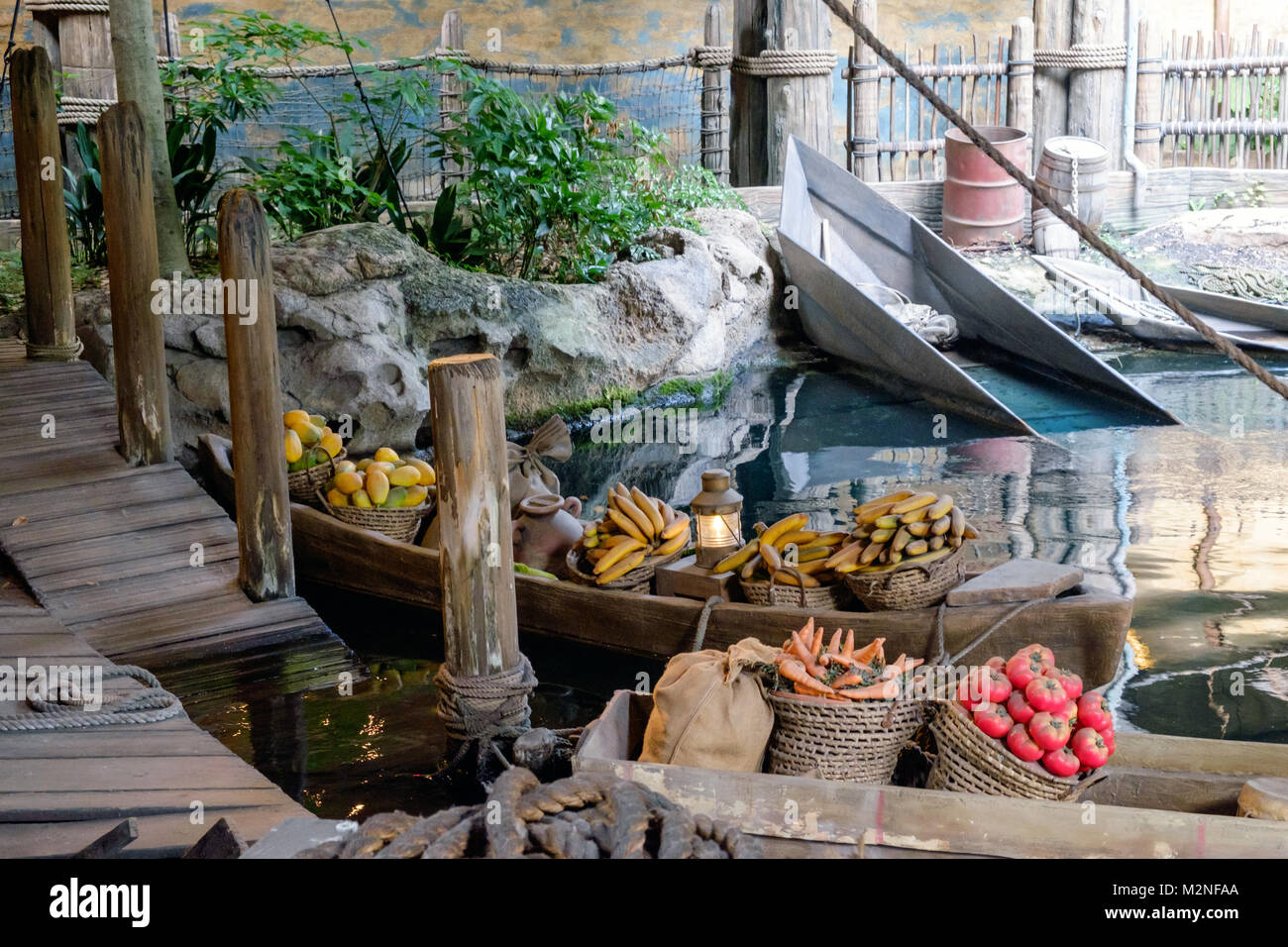 Two river boats with baskets of fruit and vegetables in the water, docked at the pier. Old wooden dock and pilings. Two empty boats in background. Pic Stock Photo
