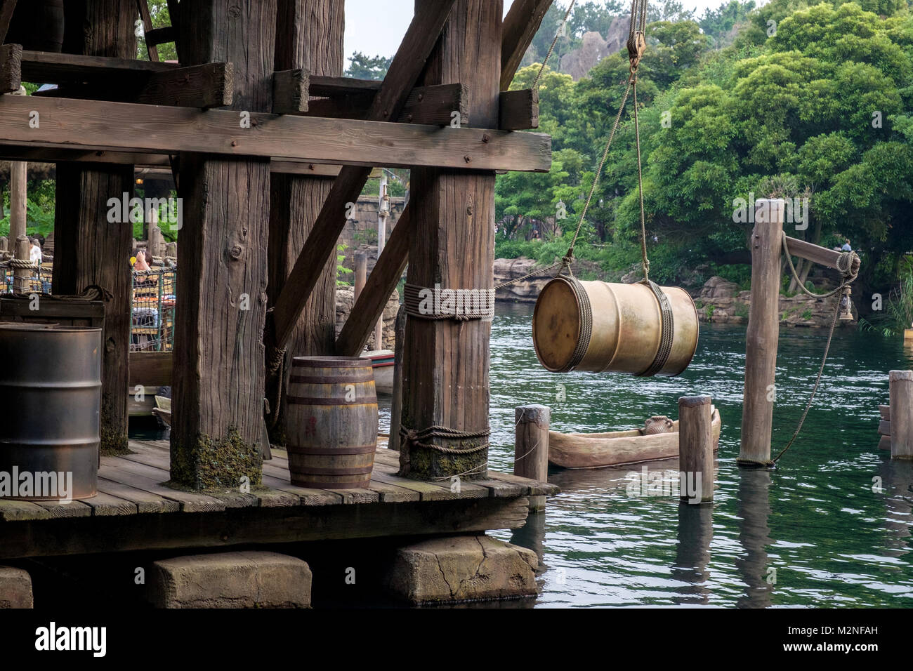Old weathered wooden dock with retro wooden barrels and beams. Old ropes, metal container hanging over the water by a rope with a hook and pulley. Emp Stock Photo