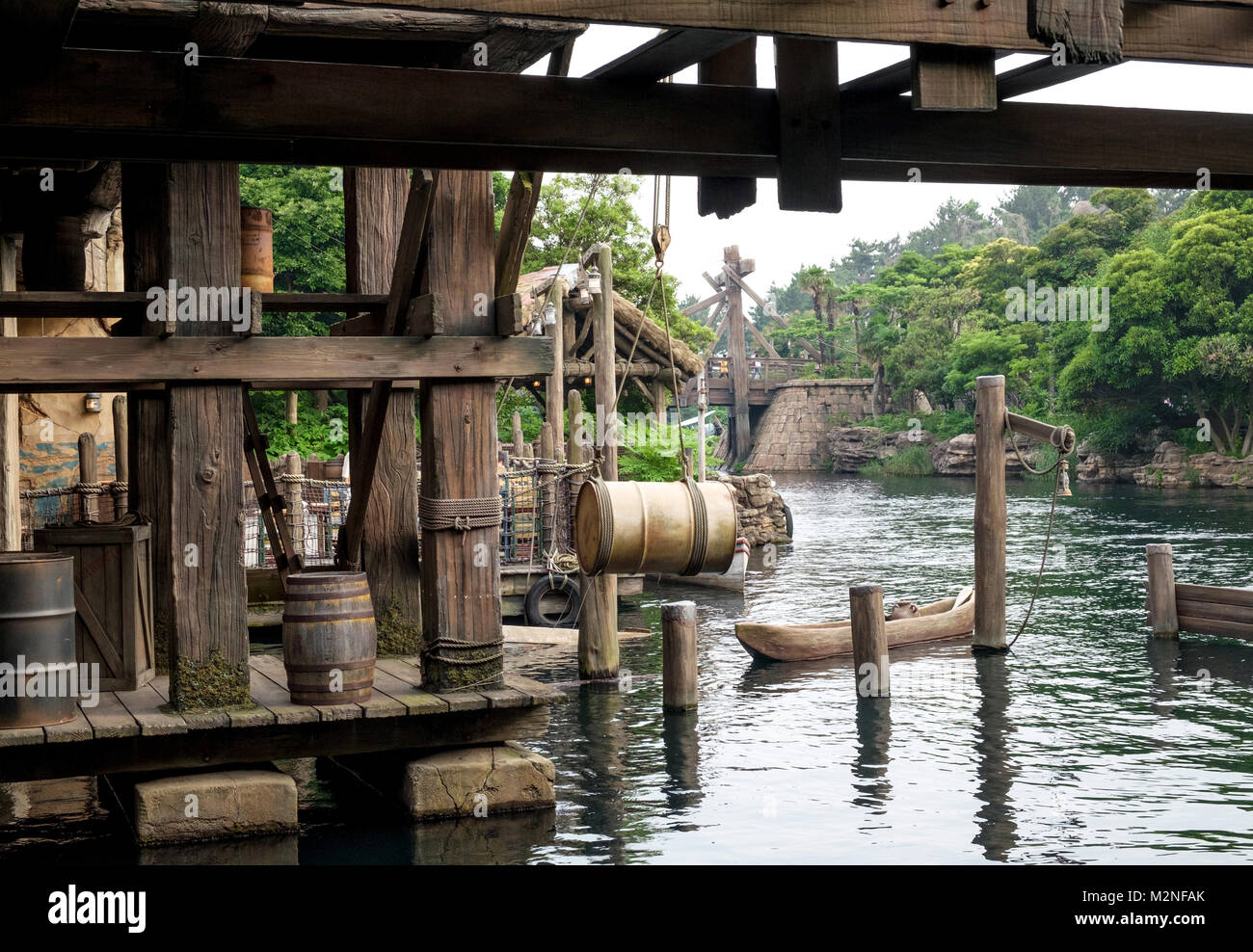 Old weathered wooden dock with retro wooden barrels and beams. Old ropes, metal container hanging over the water by a rope with a hook and pulley. Stock Photo