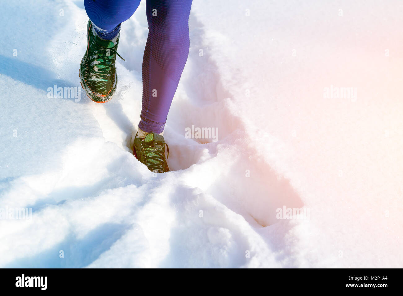 Close-up of a young woman in bright purple leggings and sneakers running through the winter snow on a bright winter day, the front view Stock Photo