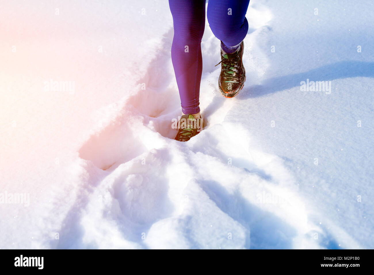 Close-up of a young woman in bright purple leggings and sneakers running through the winter snow on a bright winter day, the front view Stock Photo