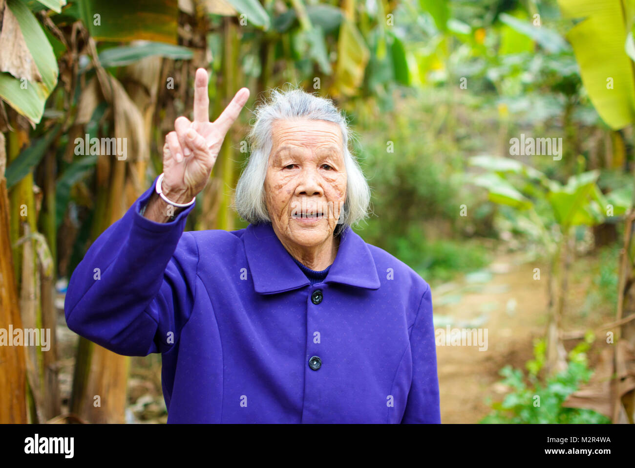 Cheerful senior asian woman showing V gesture outdoors Stock Photo