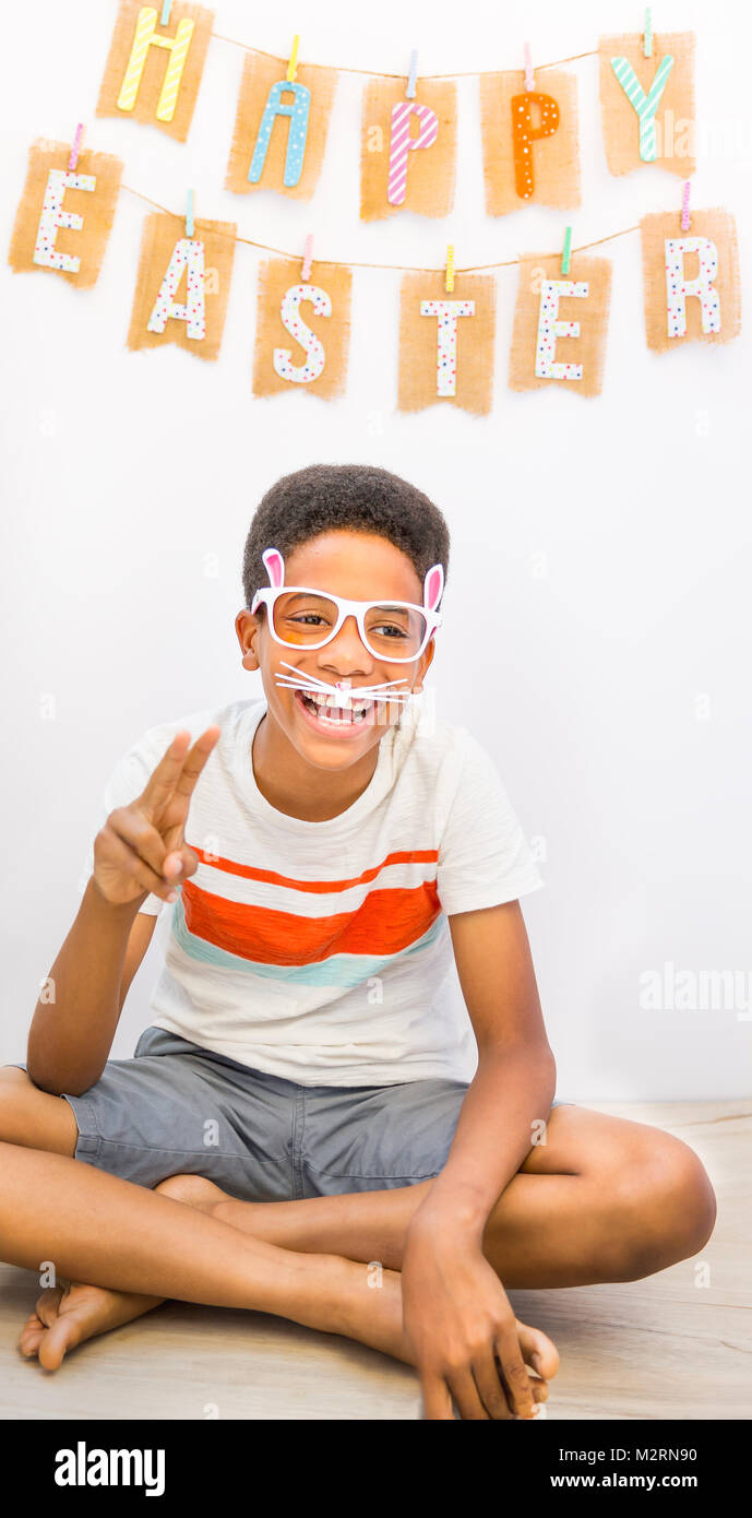 Cute African American black boy wearing bunny rabbit sunglasses with ears laughing while making the peace symbol with his fingers. Happy Easter banner Stock Photo