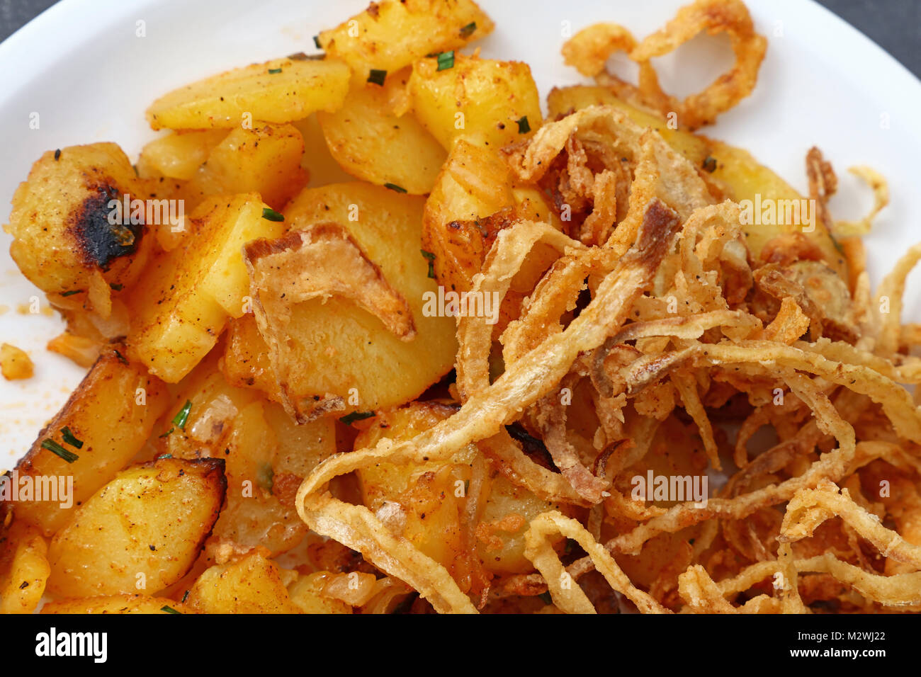 Close up portion of roasted potato and fried onion rings on white plate over grey table, elevated top view, directly above Stock Photo