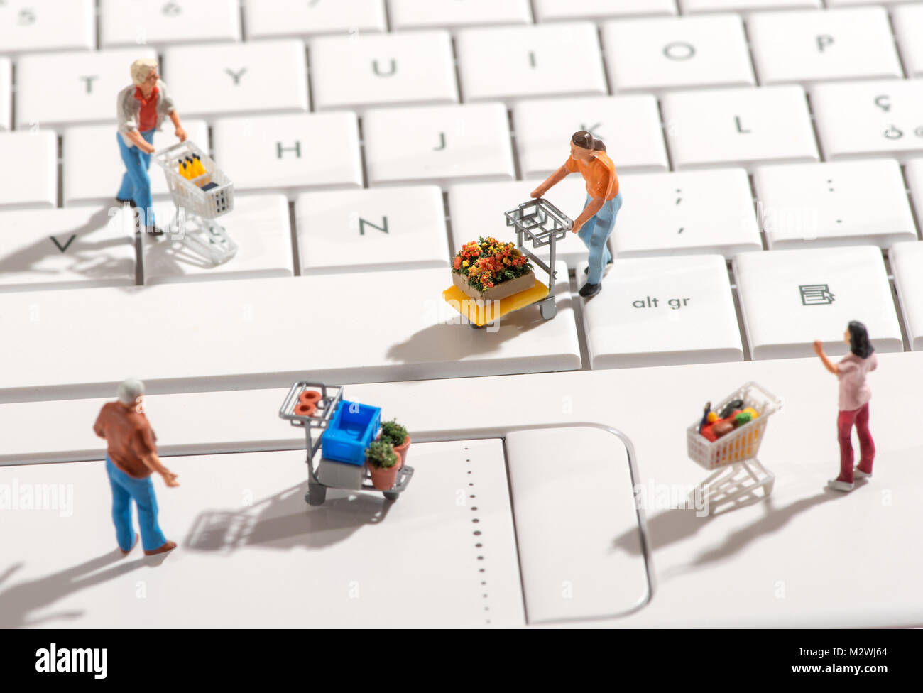 Four different miniature people with shopping carts on a white computer keyboard viewed high angle with shadows in a concept of online or internet sho Stock Photo