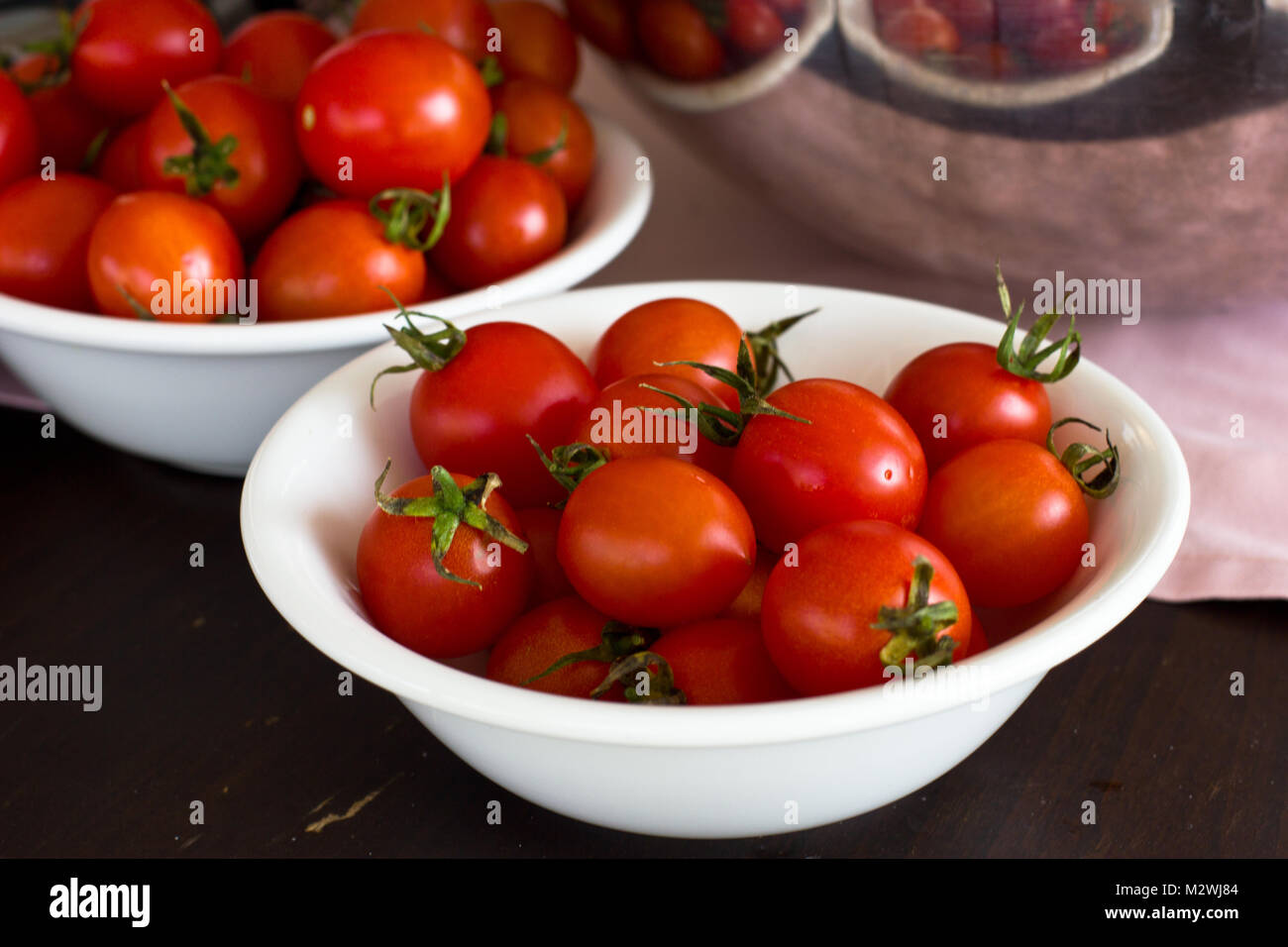 Whole cherry tomatoes in a white porcelain bowl on brown wooden table ...