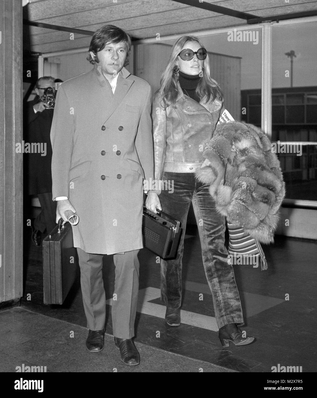 In trouser suit and carrying a fur coat, American-born actress Sharon Tate arrives with her husband Roman Polanski, at Heathrow Airport, London, from Venice to attend the premiere of her film 'Rosemary's Baby'. Stock Photo