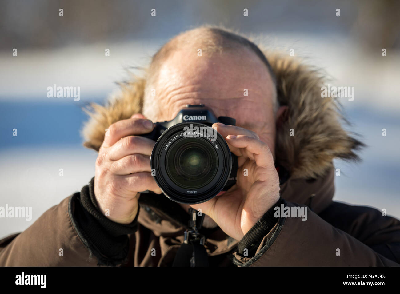 Norway, february 3, 2018: A male photographer in winter clothing is holding a Canon camera with the Canon 24-70mm 2,8 L II lens. Shallow depth of field, outdoors in snowy winter. Stock Photo