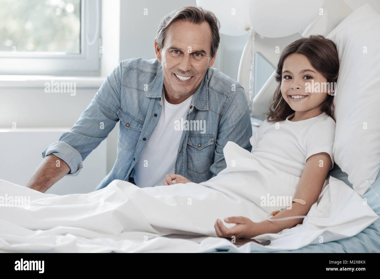 Loving father sitting next to his adorable daughter in hospital Stock Photo
