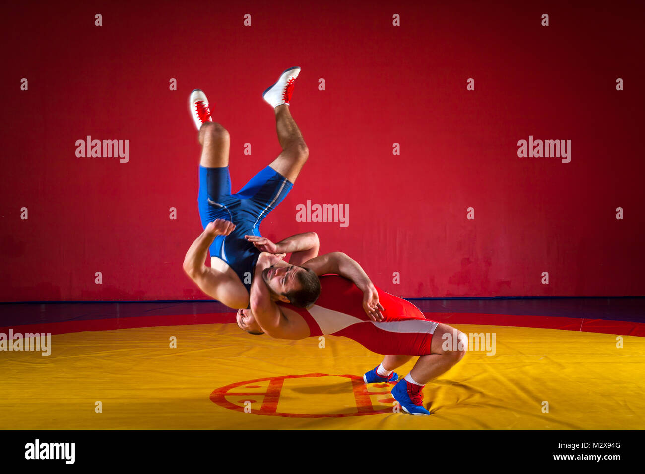 Two young men in blue and red wrestling tights are wrestlng and making