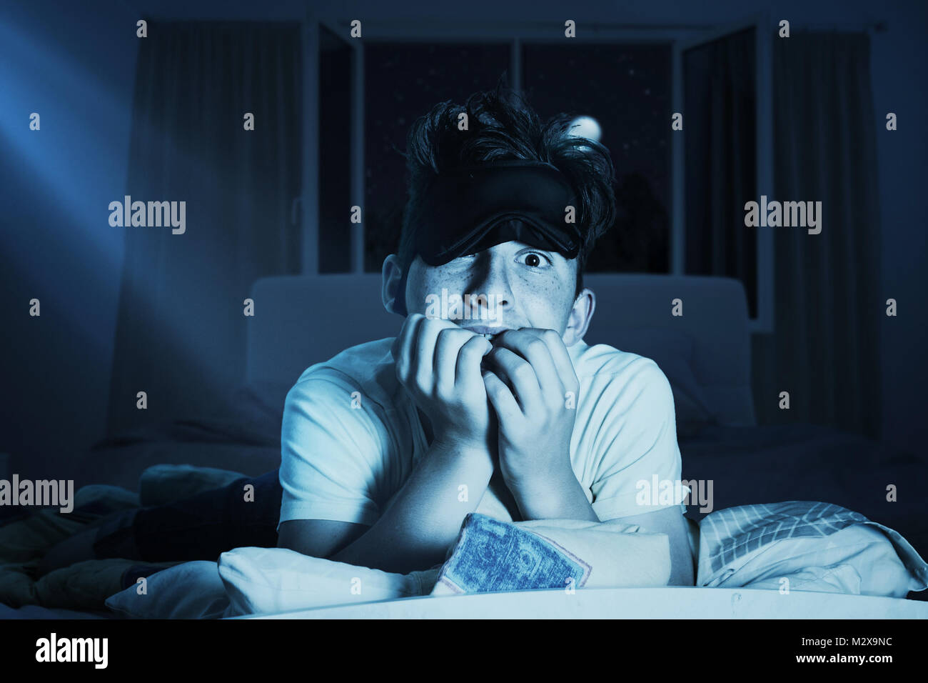 scared and sleepless boy chewing fingernails at bedroom in front of shiny moon Stock Photo