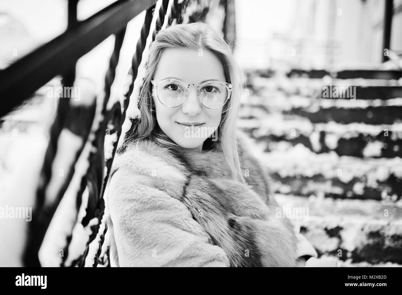 Portraiy of blonde girl in glasses, red fur coat and scarf at winter day. Stock Photo