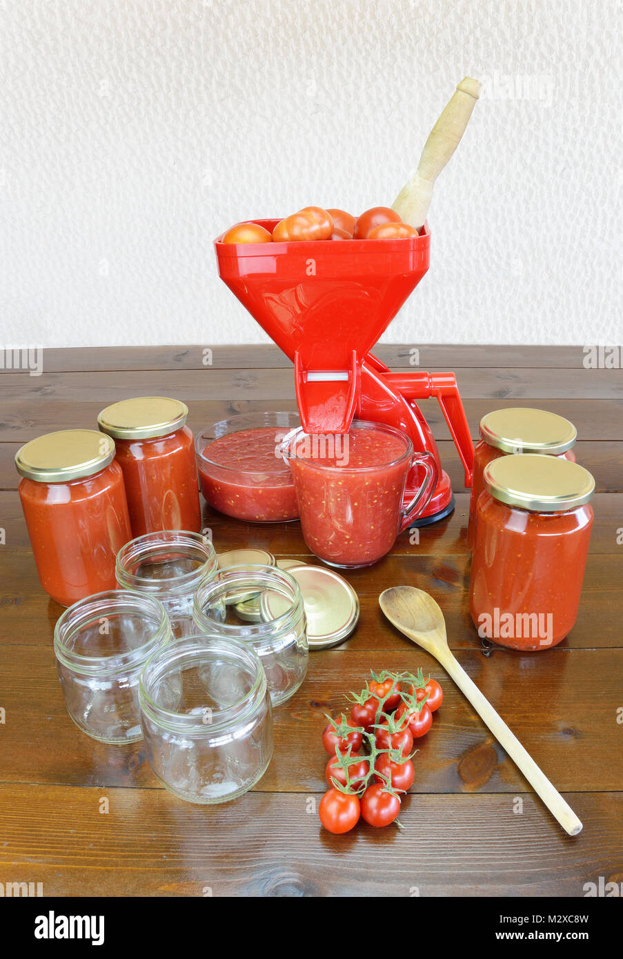 Tomato strainer, fresh crushed tomato sauce, empty and full jars, wooden spoon and fresh cherry