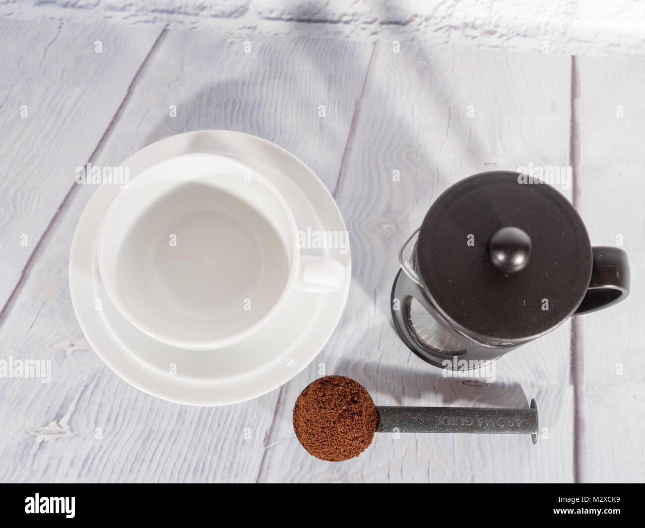 A white coffee cup with a cafetiere and a measure of ground coffee