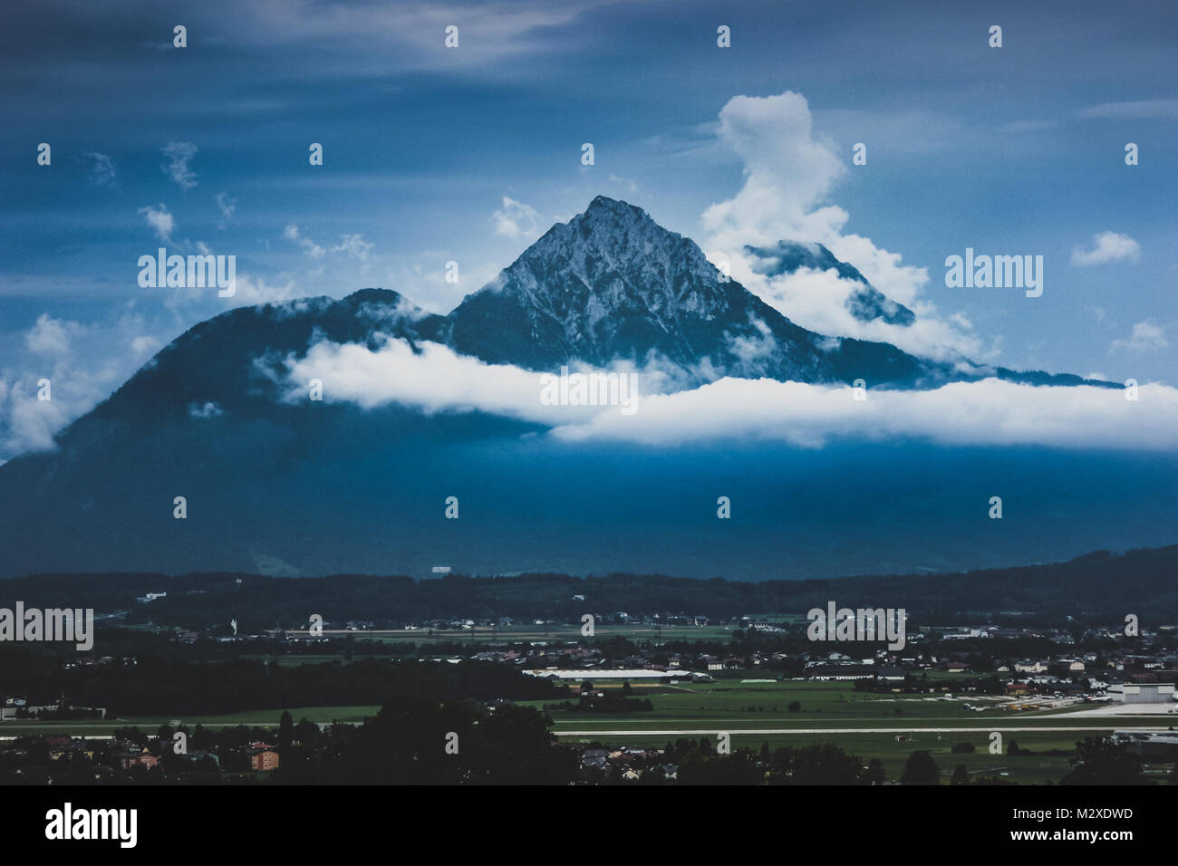 Snow-capped Hochstaufen and Zwiesel Mountain Peaks with a layer of clouds surrounding the mountain tops on an overcast day Stock Photo