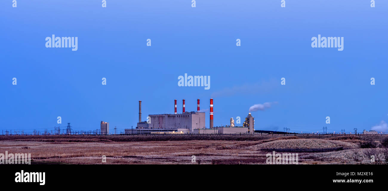 Building of a power plant with smoking pipes and glowing lights with pillars with a line of high-voltage gears against a blue sky in the background, a Stock Photo