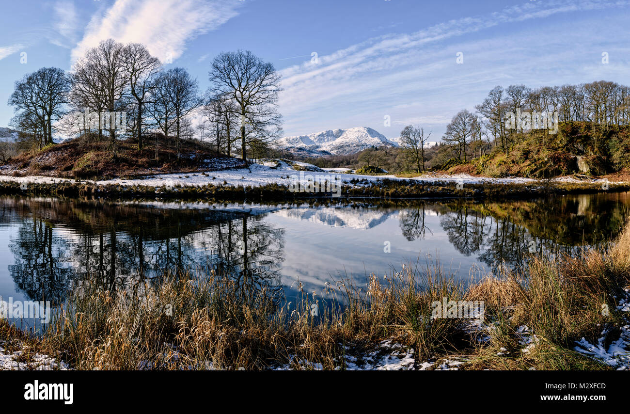 Snow-covered Wetherlam reflected in the river Brathay between Elter Water and Skelwith Bridge Stock Photo