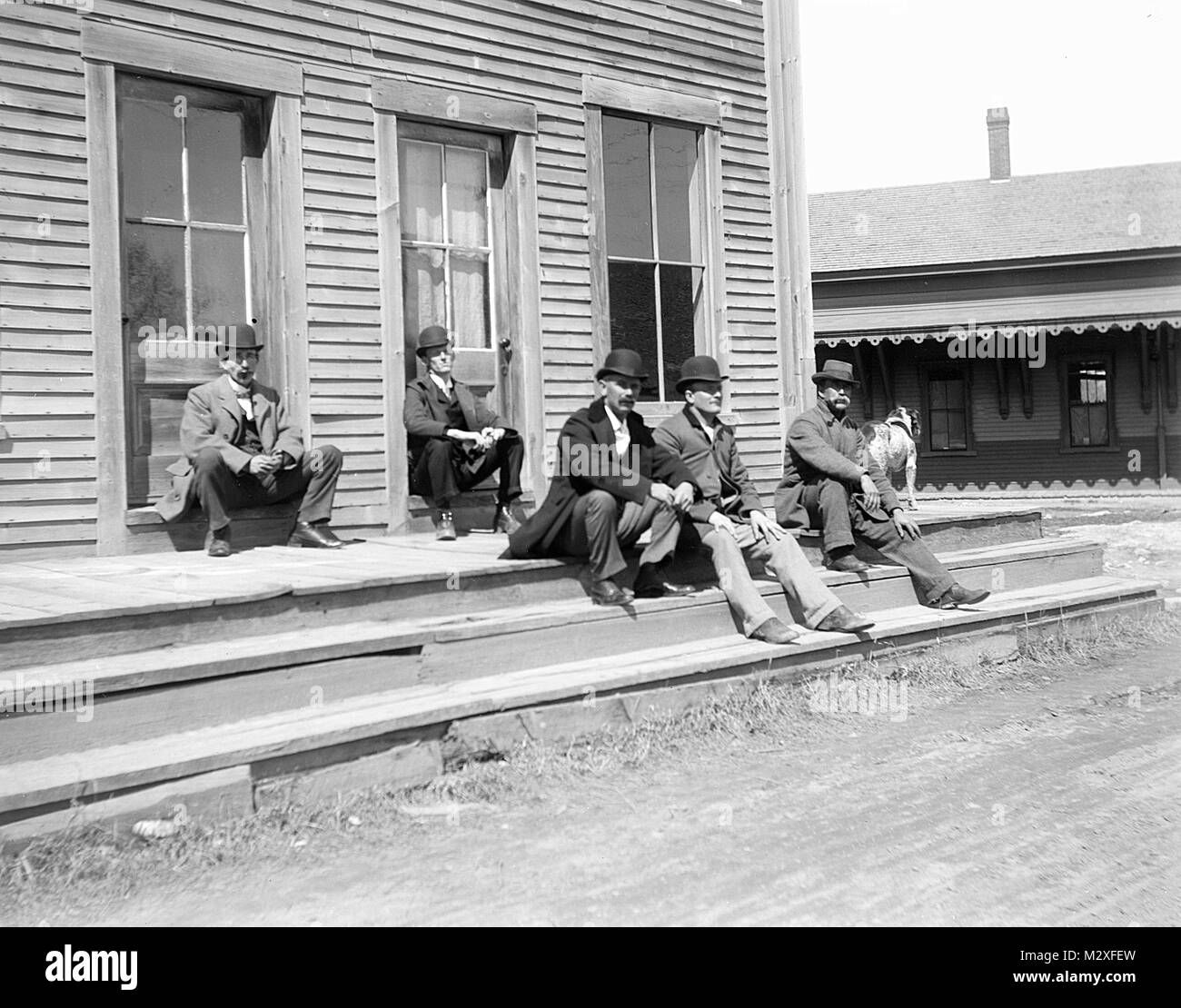 A gang of touch looking men sit on a wooden sidewalk in a western town, ca. 1890. Stock Photo