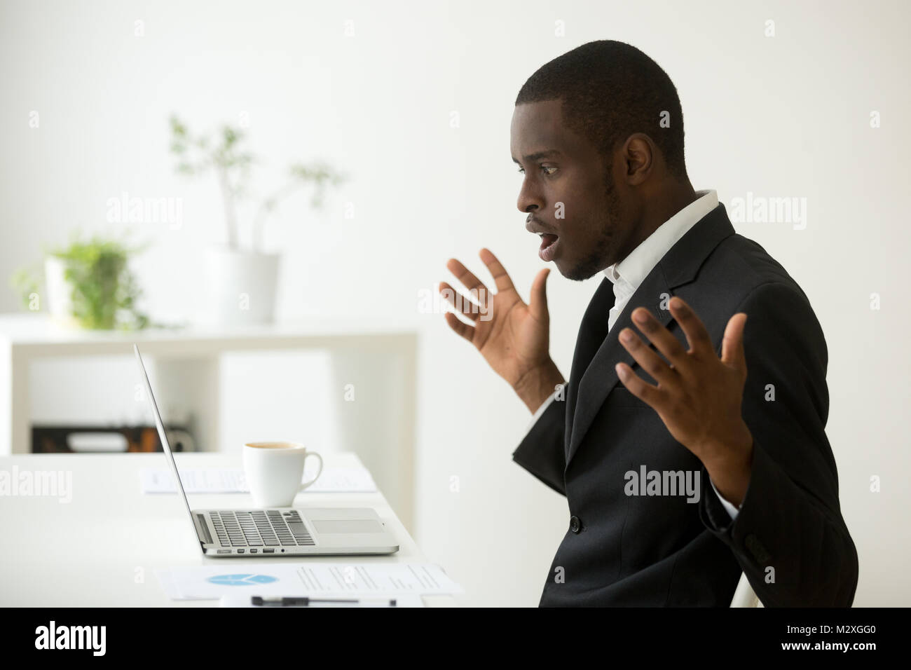 Shocked african-american businessman in suit feeling stunned by online news looking at computer screen sitting at workplace with laptop, stressed trad Stock Photo
