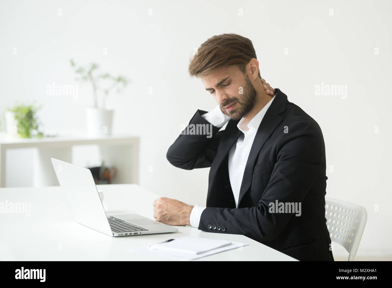 Young businessman in suit feeling neck pain after sedentary work Stock Photo