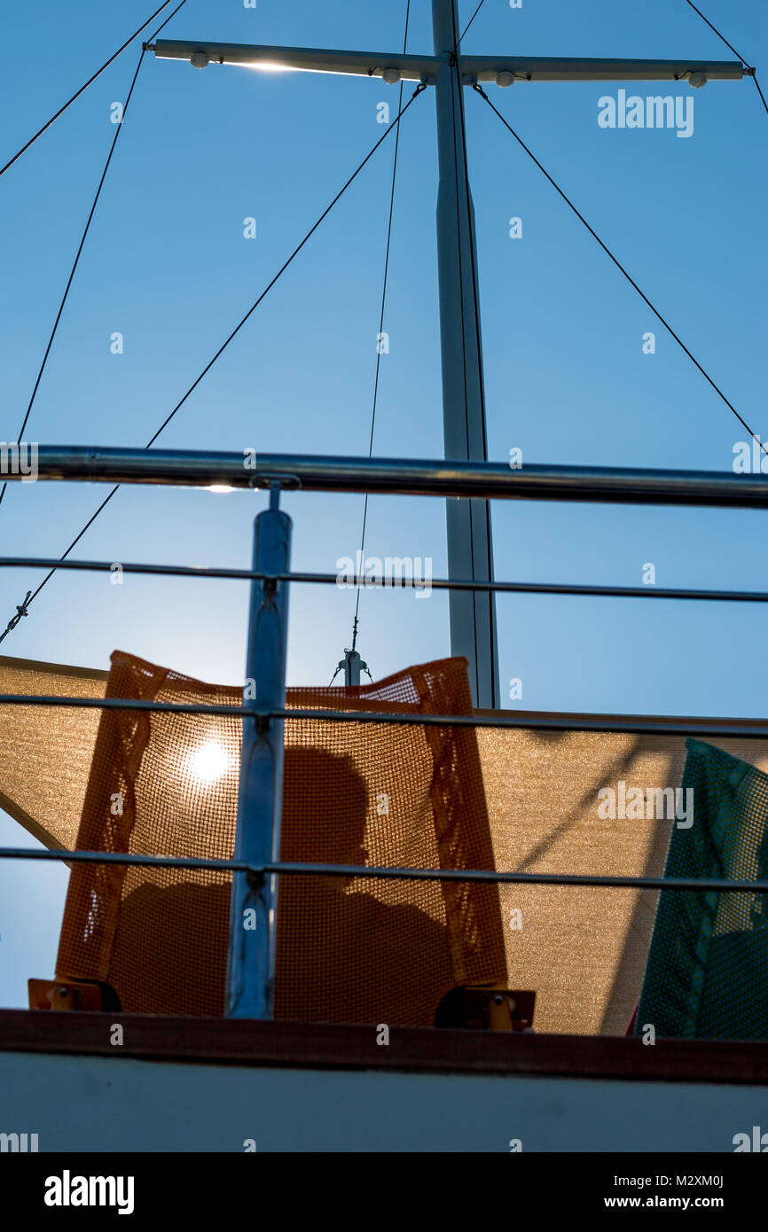 The shadow of a man sitting in a sunbed on a cruise ship against the Sun in the summer, a mast and some rigging is included in the image as well Stock Photo