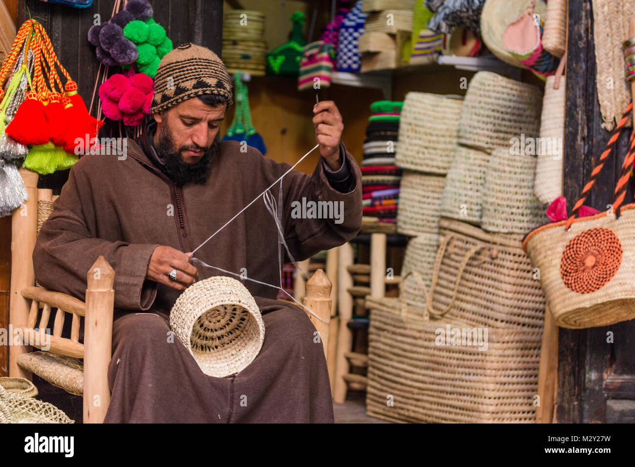 Craftsman mending a wicker basket while sitting in his shop located in the souks of Marrakesh, Morocco Stock Photo