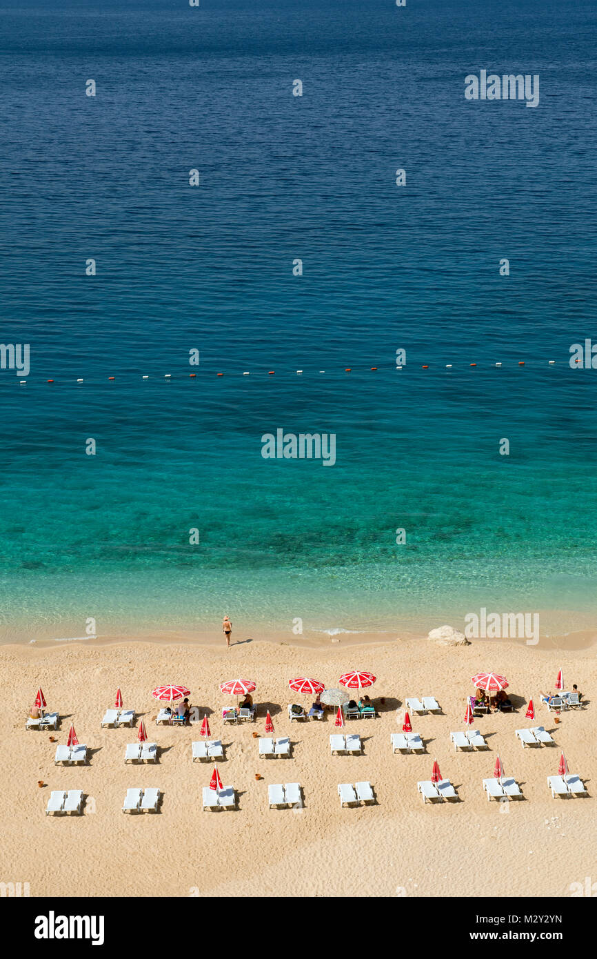 An aerial view of a beautiful beach with turquoise waters, featuring rows of sun loungers and red umbrellas neatly arranged on the sandy shore. Stock Photo