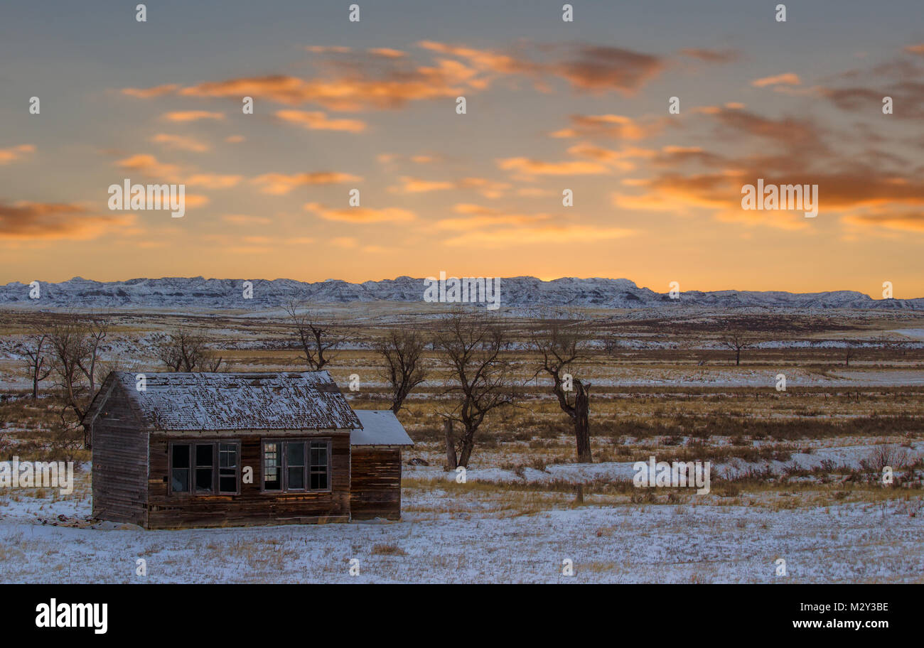 An abandoned square wooden house with broken windows in a valley with canyons in the background in a countryside Wyoming landscape in winter Stock Photo