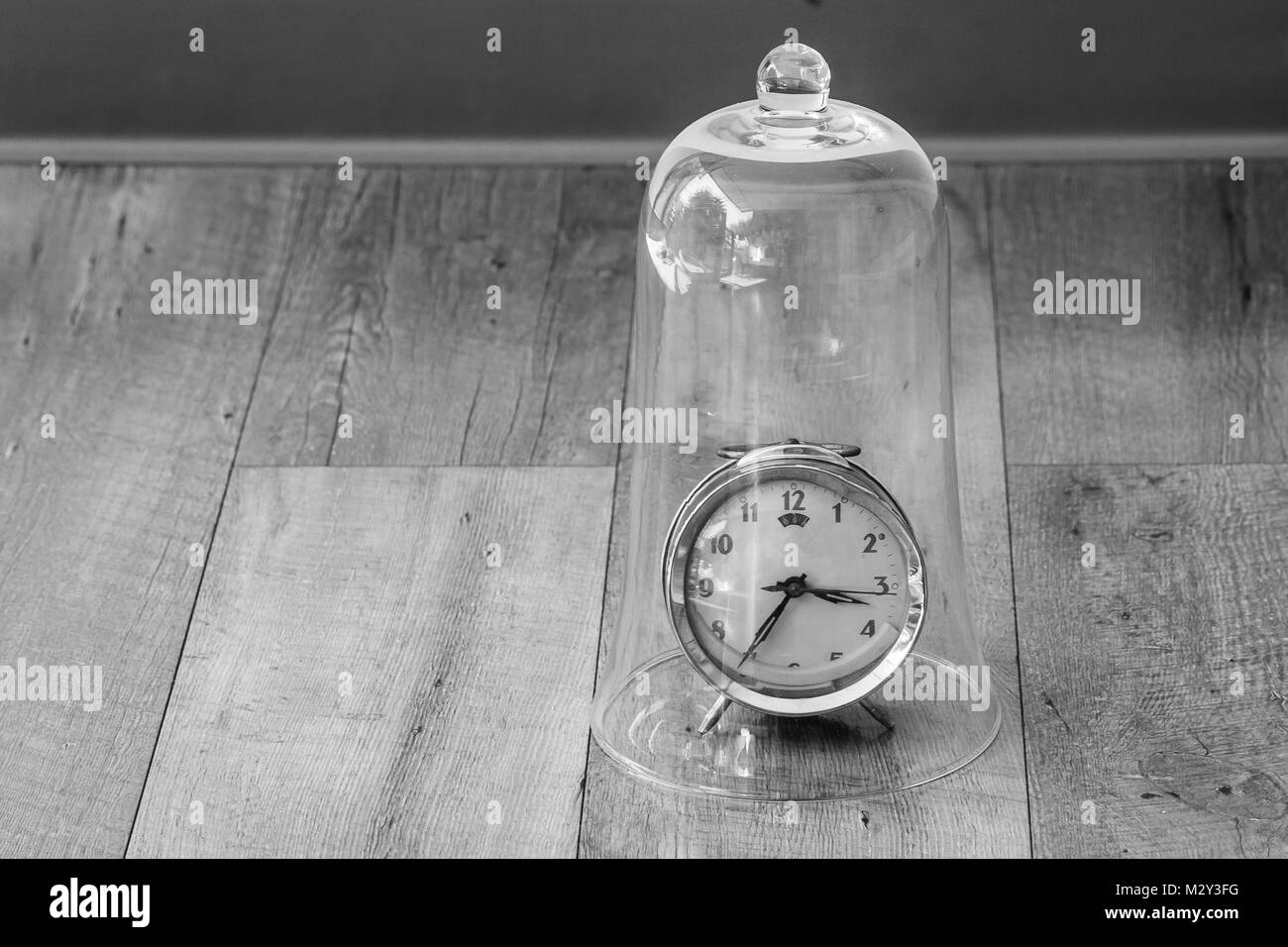 Time Management Concept : Close up red vintage alarm clock be distorted and damaged setting on wooden floor in the glass dome. Stock Photo
