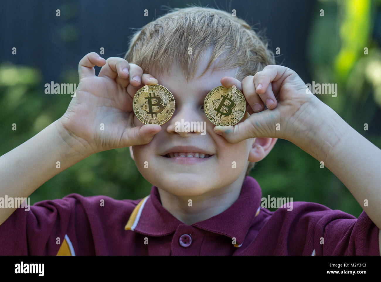 Child holding Bitcoins over his eyes Stock Photo