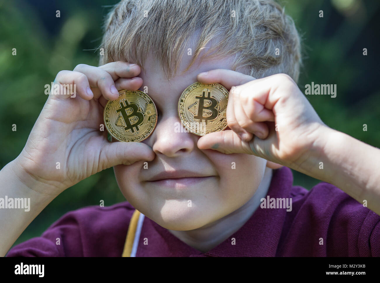 Boy holding Bitcoins up to his eyes Stock Photo