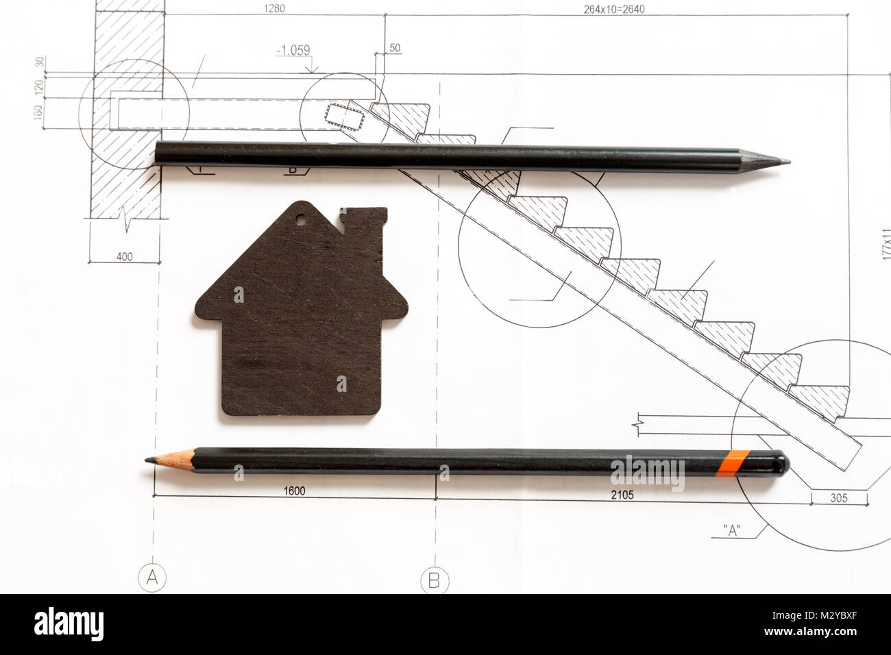 Image of small black model of a house with black pencils lying on a blueprint background Stock Photo