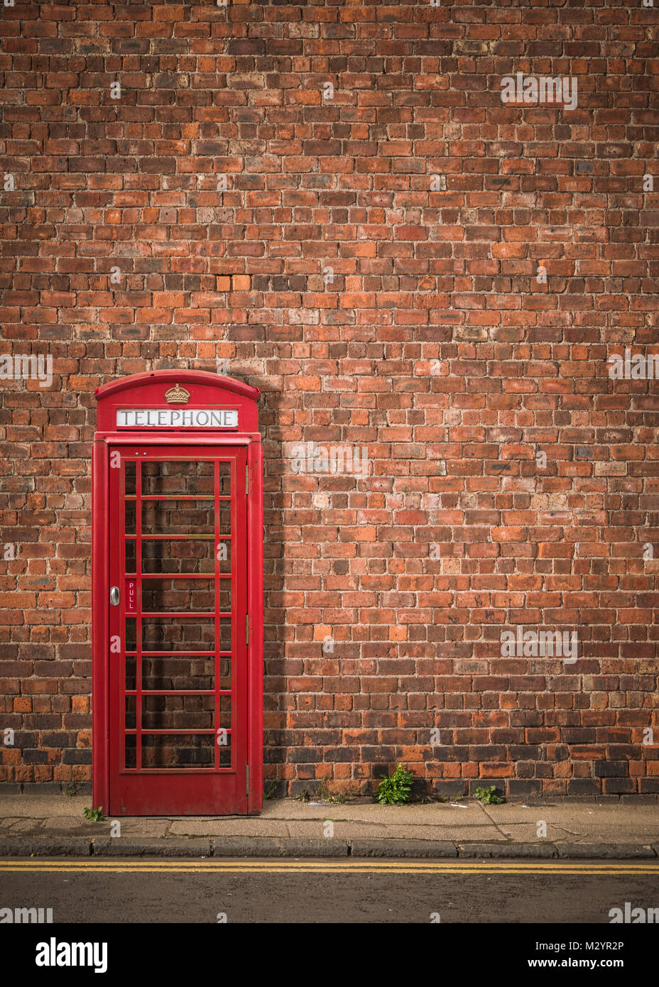 Traditional Red British Telephone Box Against A Red Brick Wall With Copy Space Stock Photo
