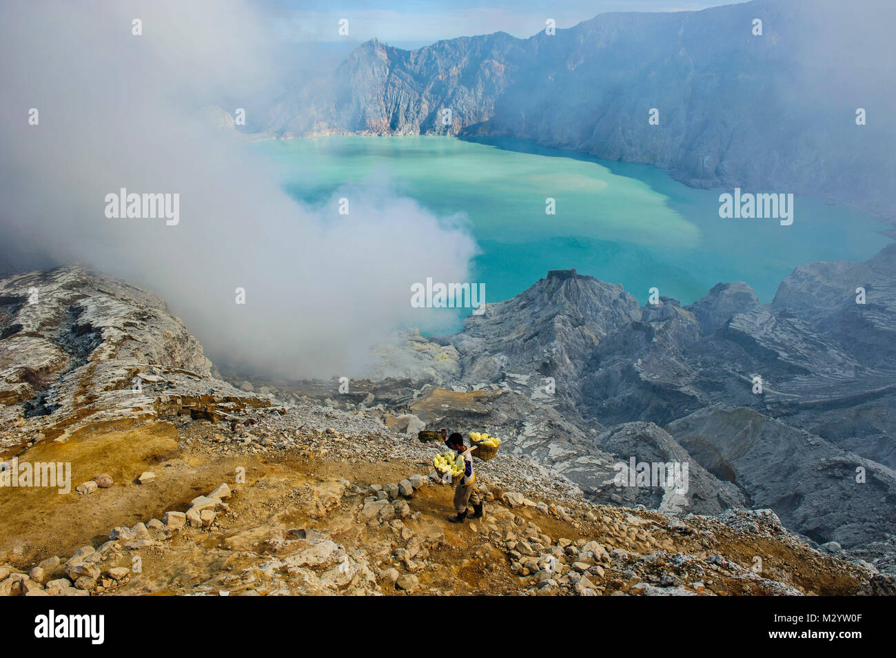 Worker loaded with big pieces of sulphur before the steam clouds on the Ijen crater lake, Java, Indonesia Stock Photo