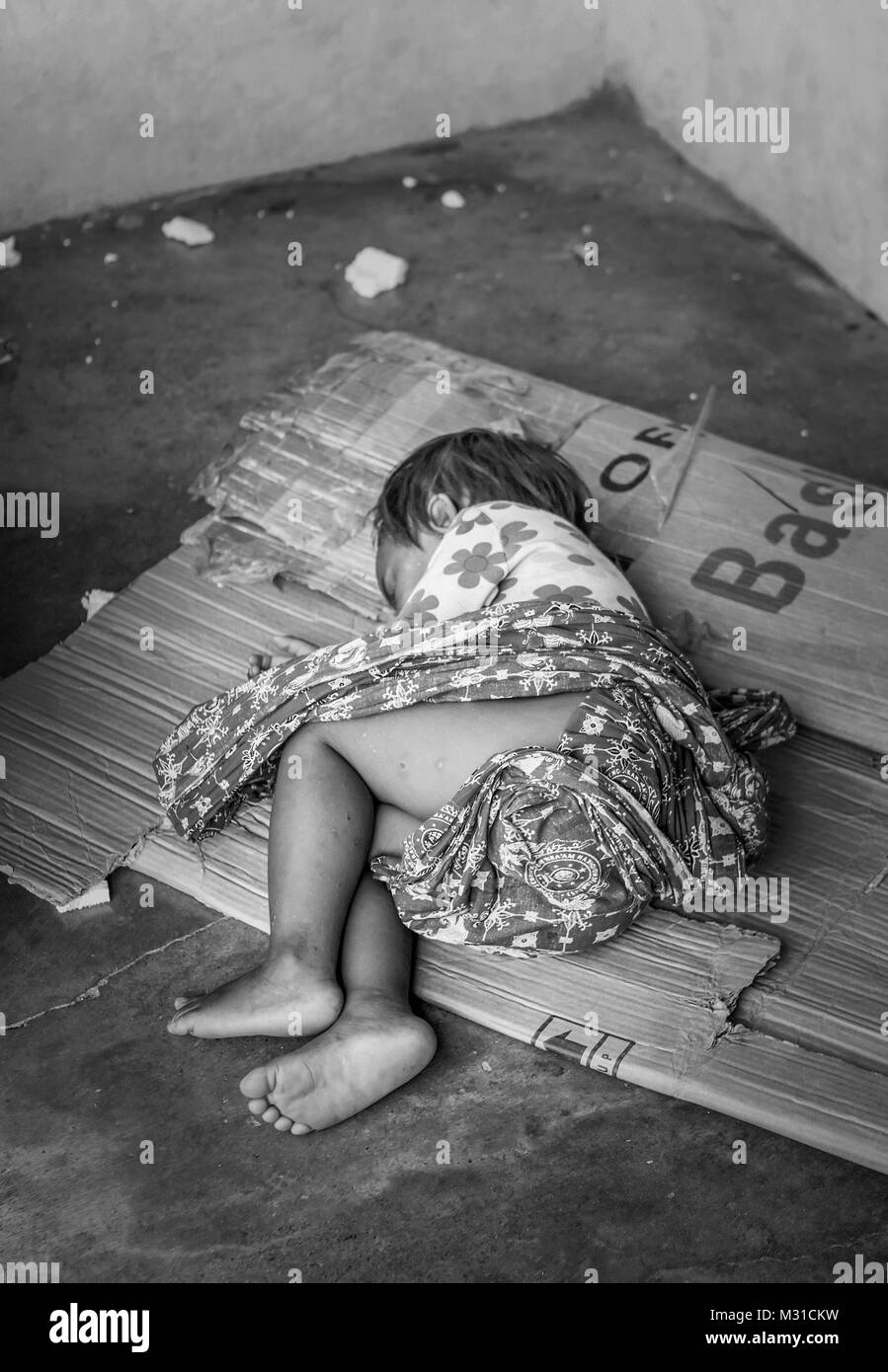 A homeless Filipino child about 2 - 3 years old sleeps on a piece of cardboard on the floor of a bus stop. Stock Photo