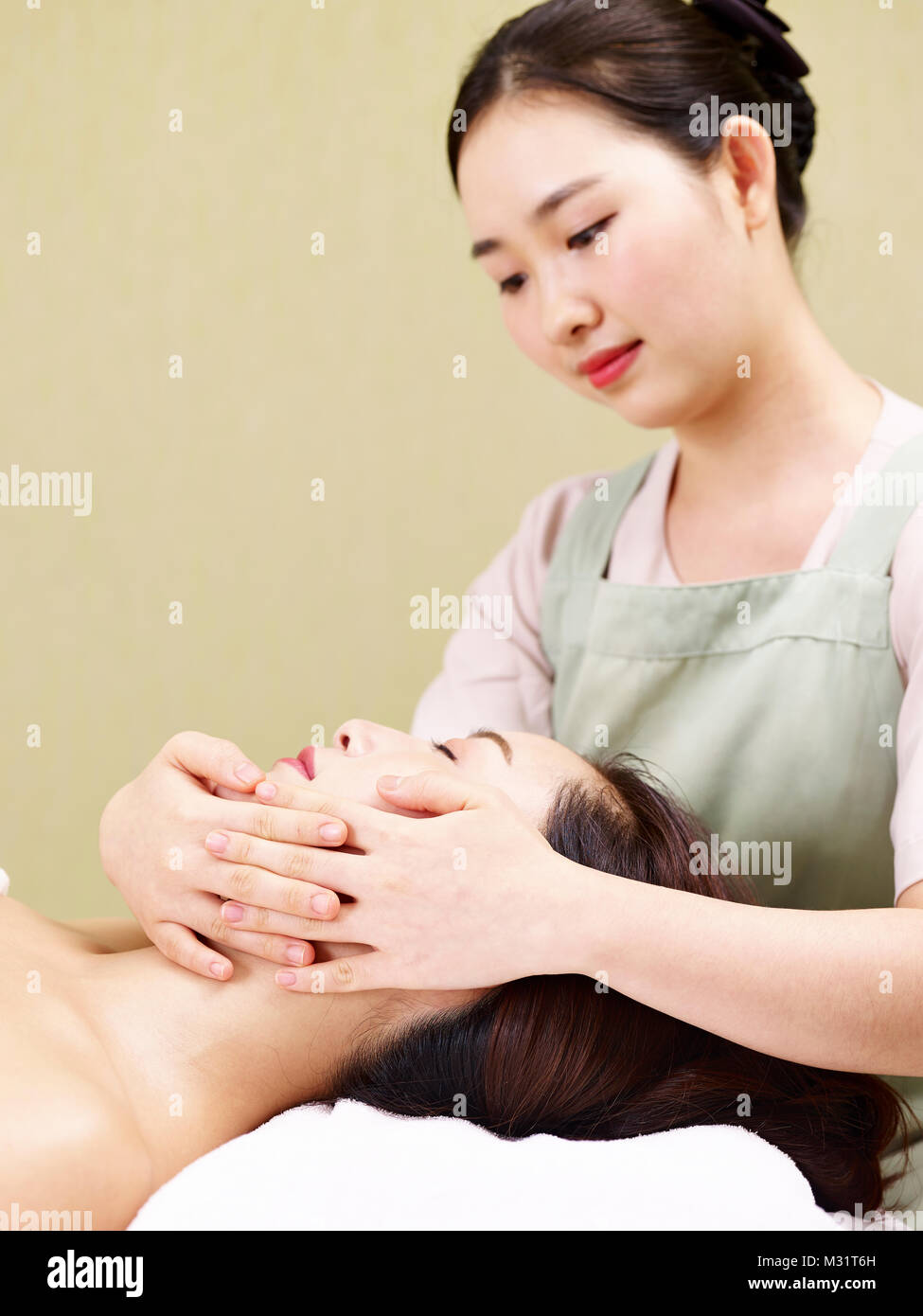 young asian masseur performing face massage on woman in spa salon Stock Photo