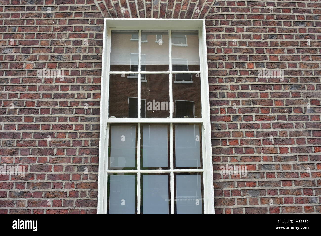 Multipane window with white frame in brick wall reflecting building on