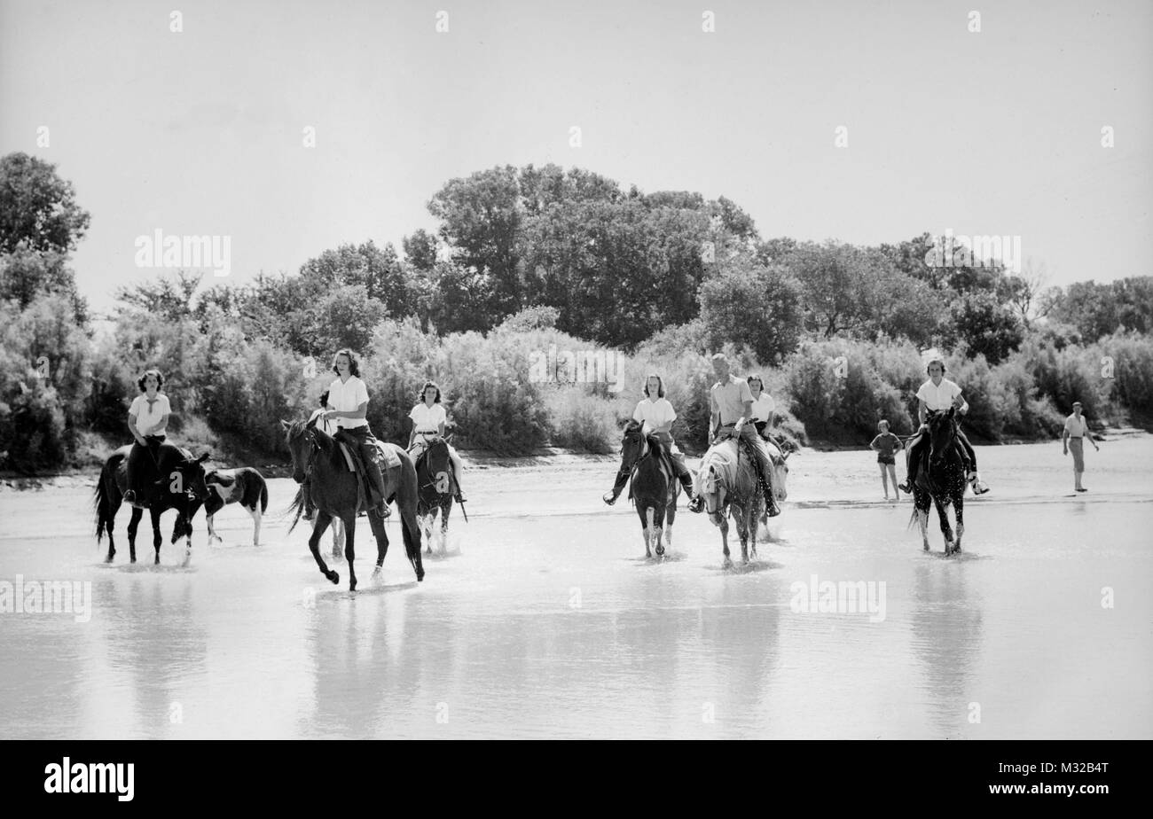 Group of women ride horses along a riverbed in the American West, ca. 1950. Stock Photo