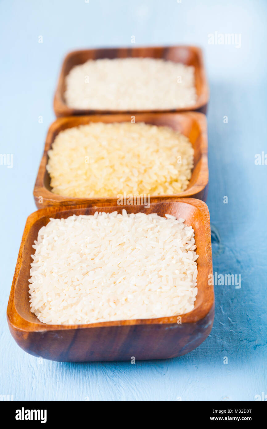 Three bowls with different varieties of rice on a wooden background