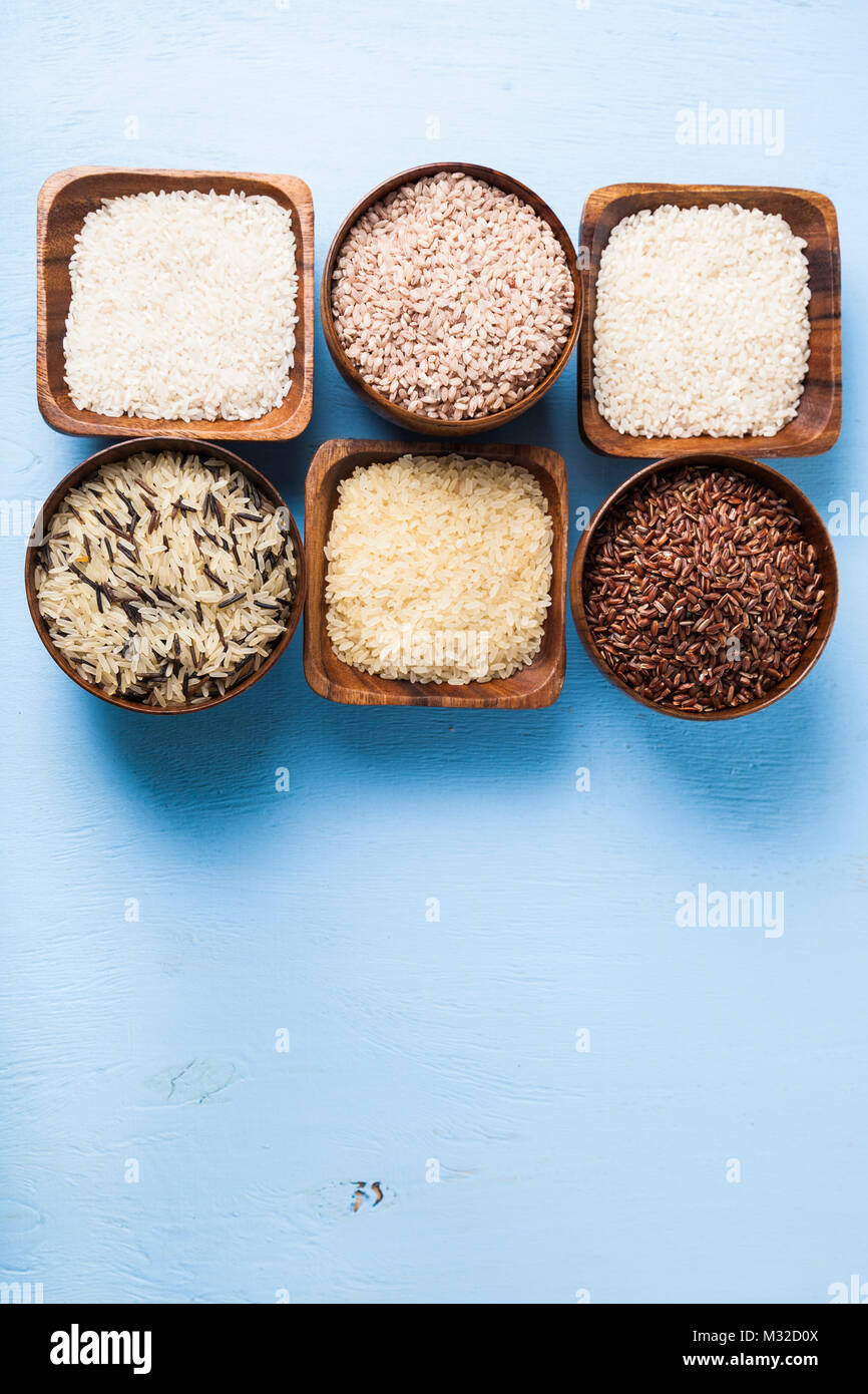 Six bowls with different varieties of rice on a wooden background
