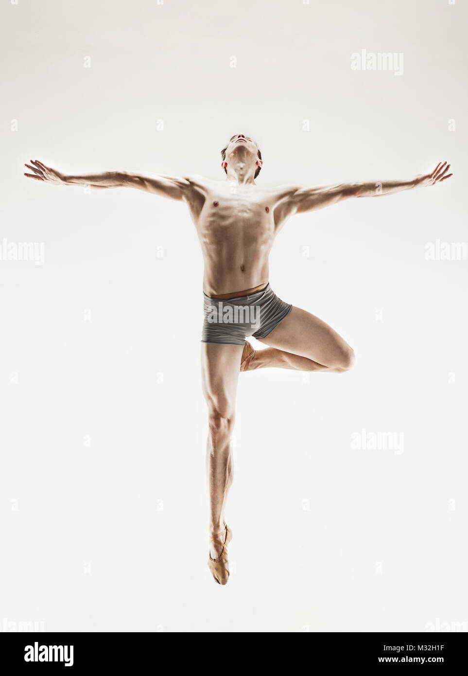 Athletic ballet dancer in a perfect shape performing over the grey ...