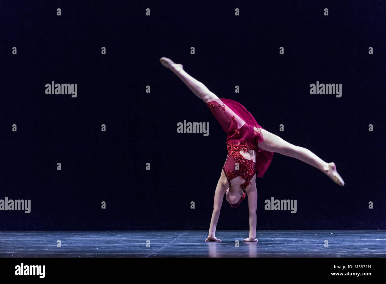 Twelve year old girl performing a solo lyrical dance onstage, doing a cartwheel to the floor Stock Photo