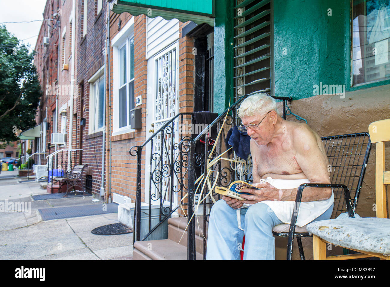 Philadelphia Pennsylvania,South Philly,street,sidewalk,man men male,senior seniors citizen citizens,barechest,sitting,reading,white hair,outdoor,row h Stock Photo