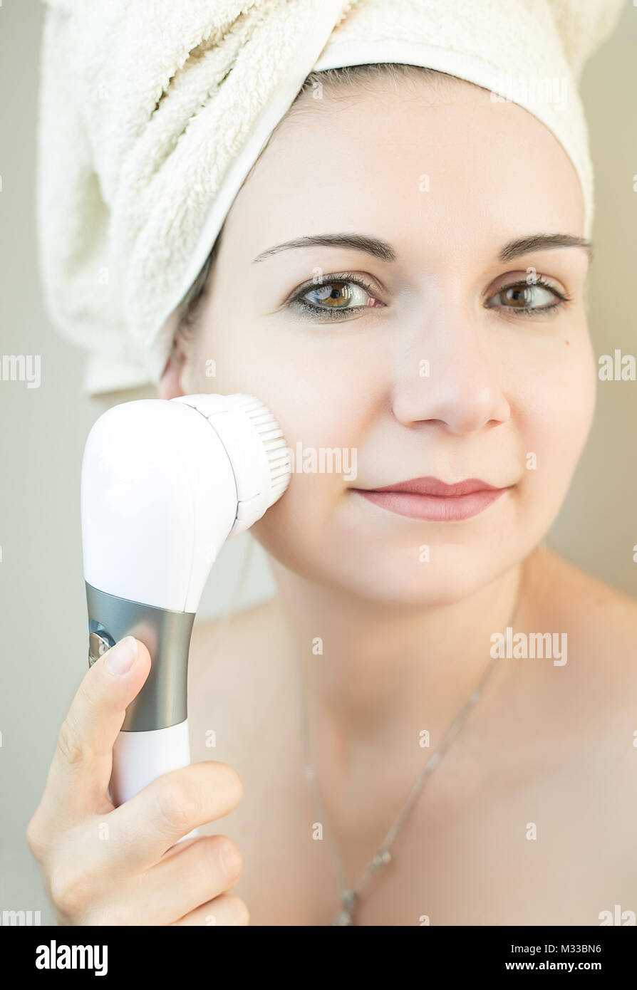 Beautiful woman using a facial cleaning brush machine to clean deep her